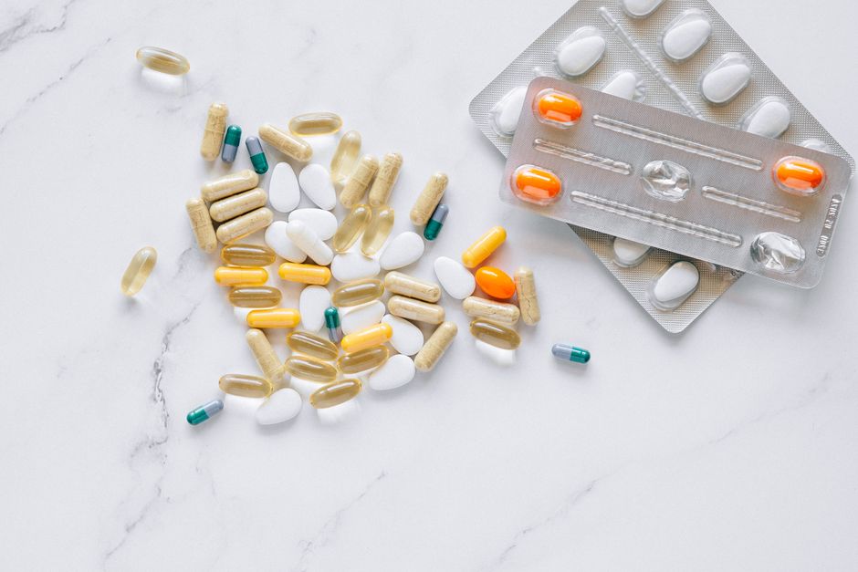 A variety of colored capsules and tablets arranged on a white marble surface, alongside blister packs.