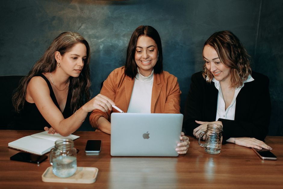 Three women in smart casual attire collaborate over a laptop in a business meeting.